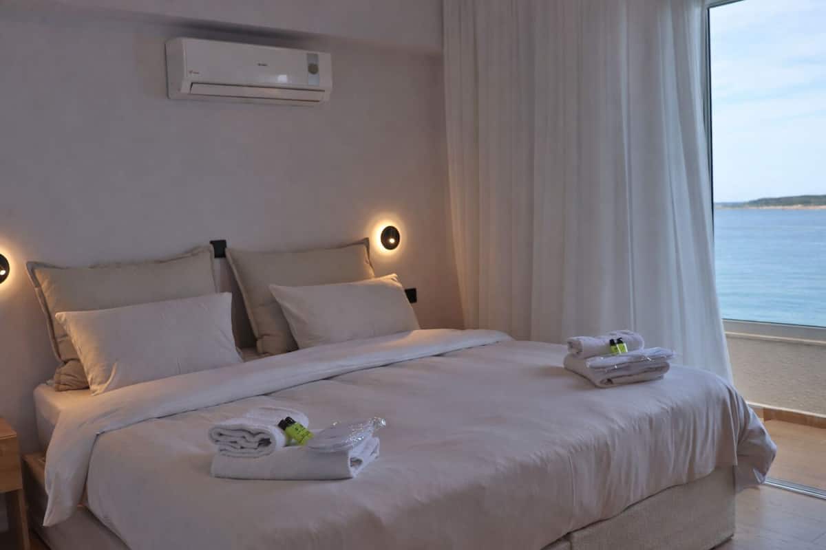 A hotel room with a bed, a nightstand, an air conditioning unit, and a view of the sea.