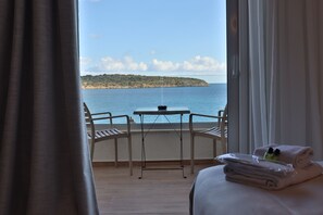 Ein Balkon mit Tisch und Stühlen, ein Bett mit Handtüchern und Blick auf das Meer sowie eine entfernte Insel.