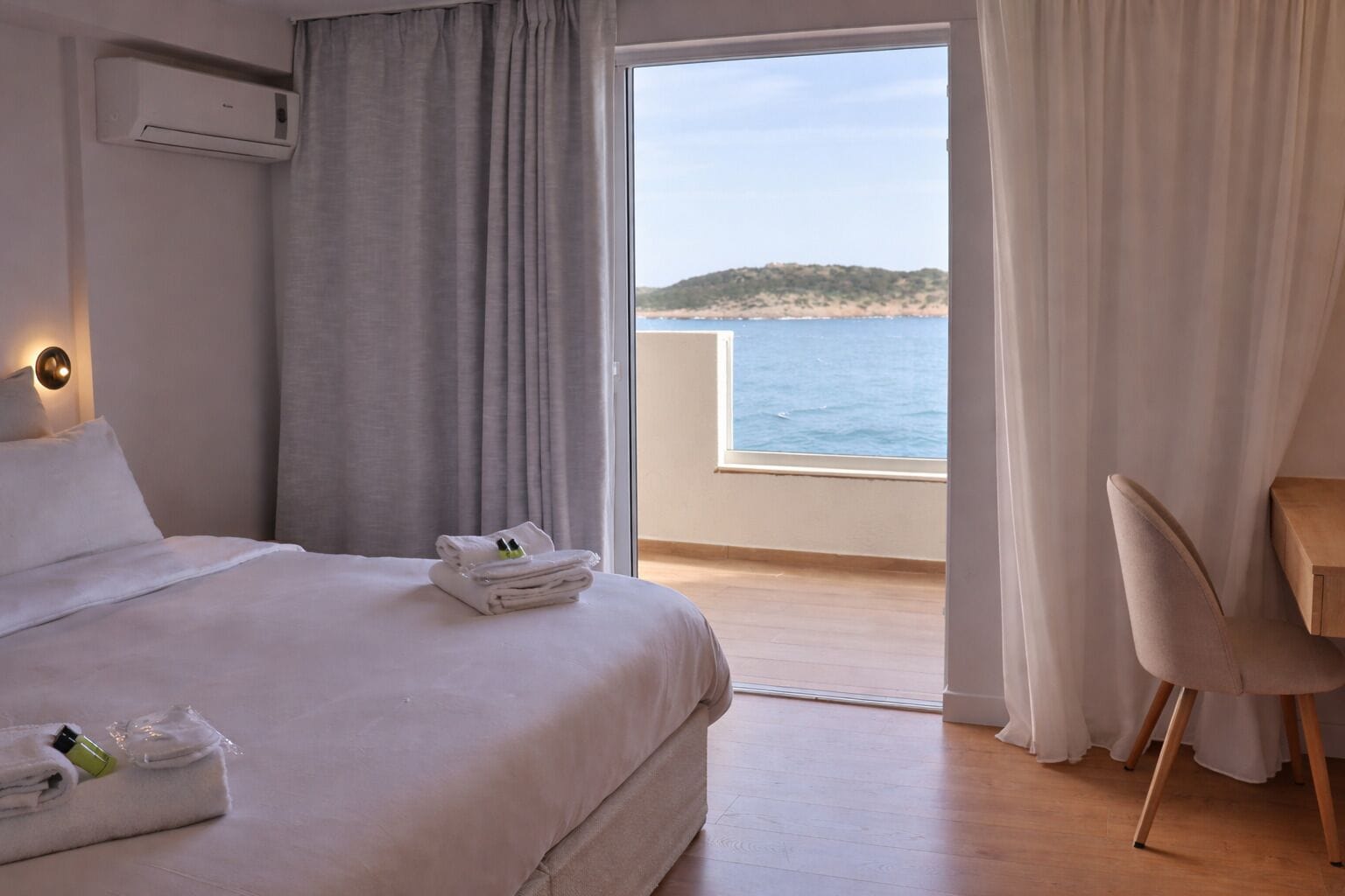 Een hotelkamer met een bed, een stoel, een tafel en uitzicht op zee.
