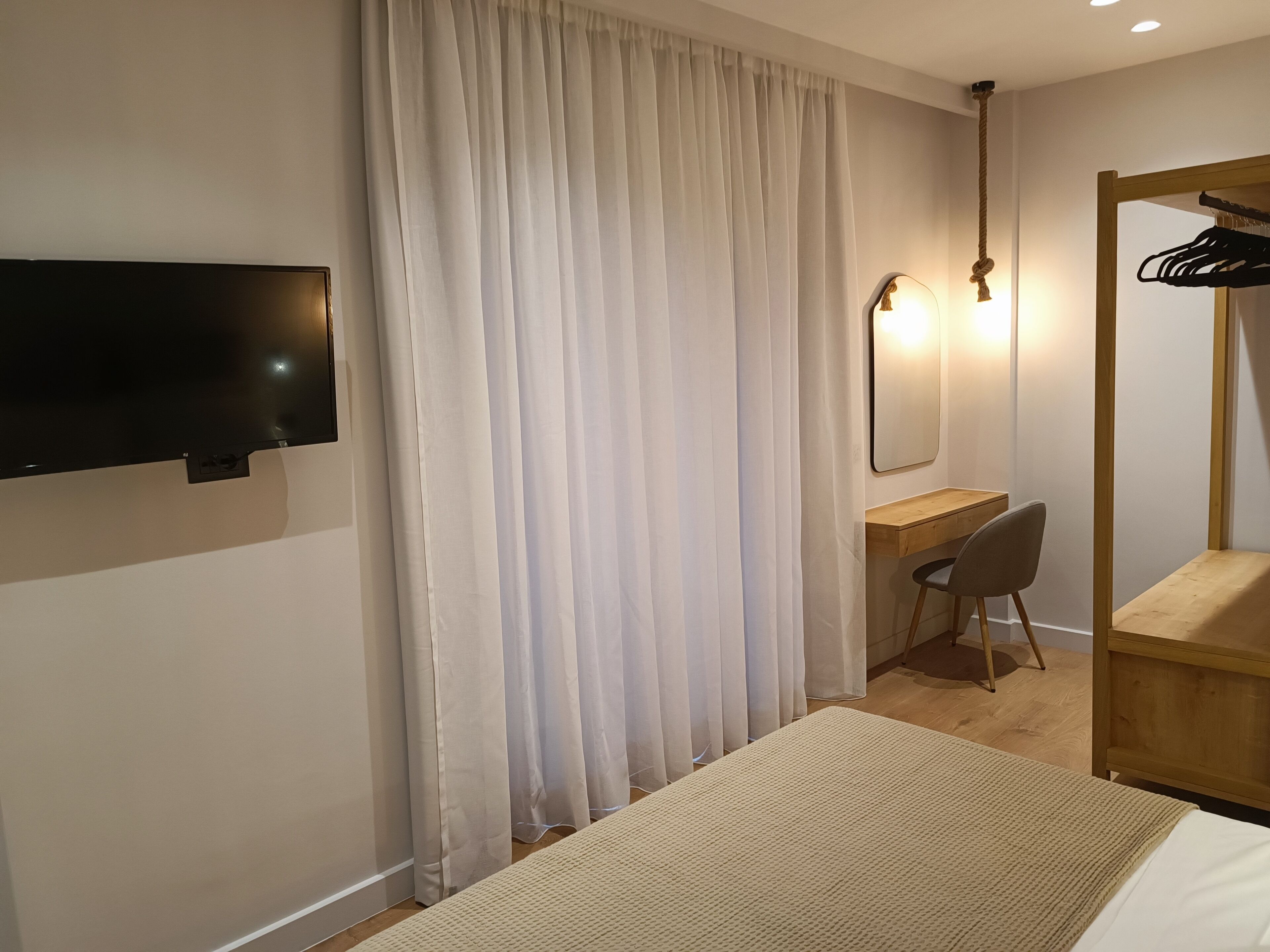 Een hotelkamer met een bed, een bureau, een stoel, een aan de muur bevestigde televisie en een houten garderobe met spiegel.