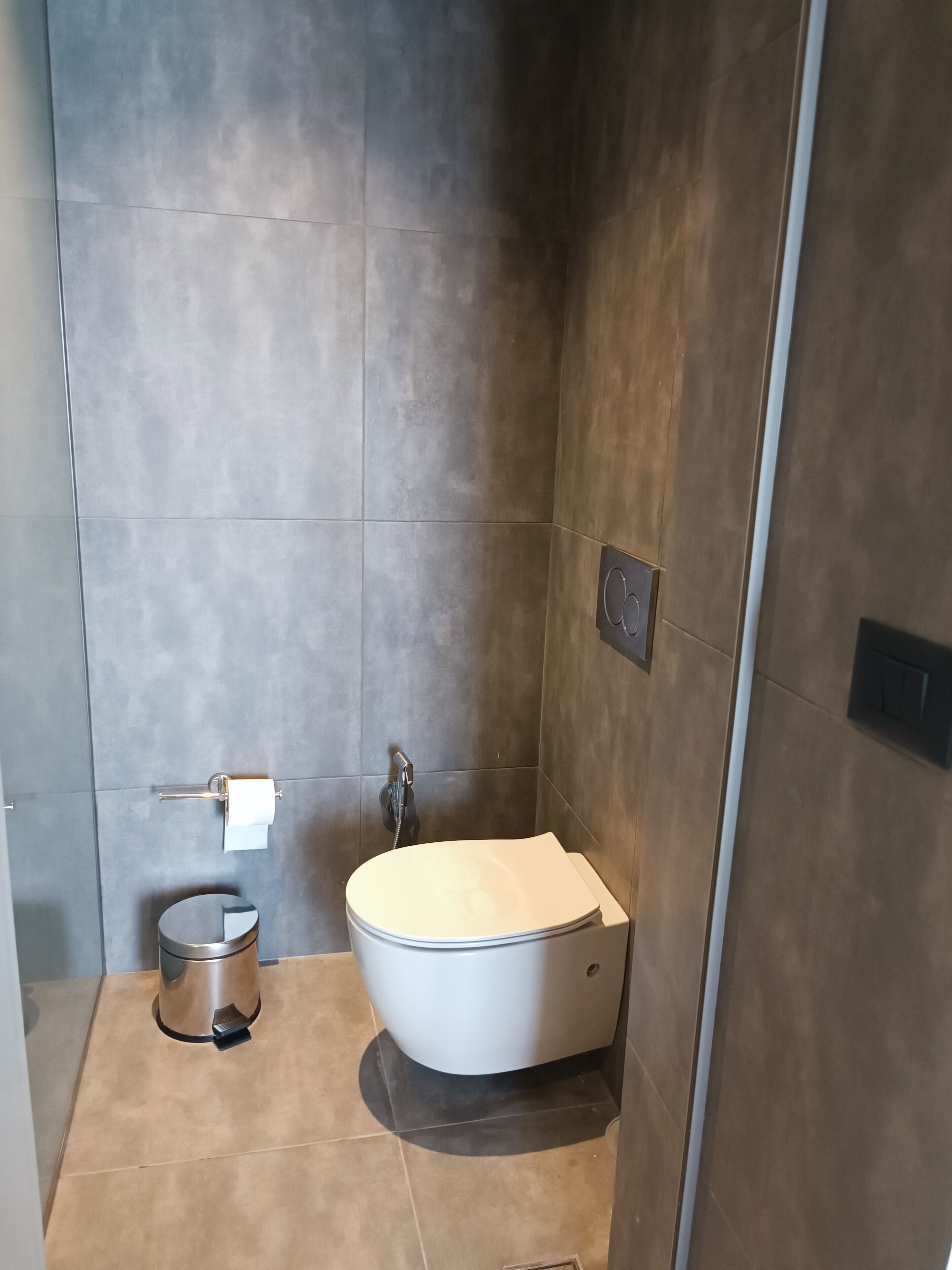 Une salle de bain moderne équipée de toilettes, d’un sèche-mains et d’une poubelle.