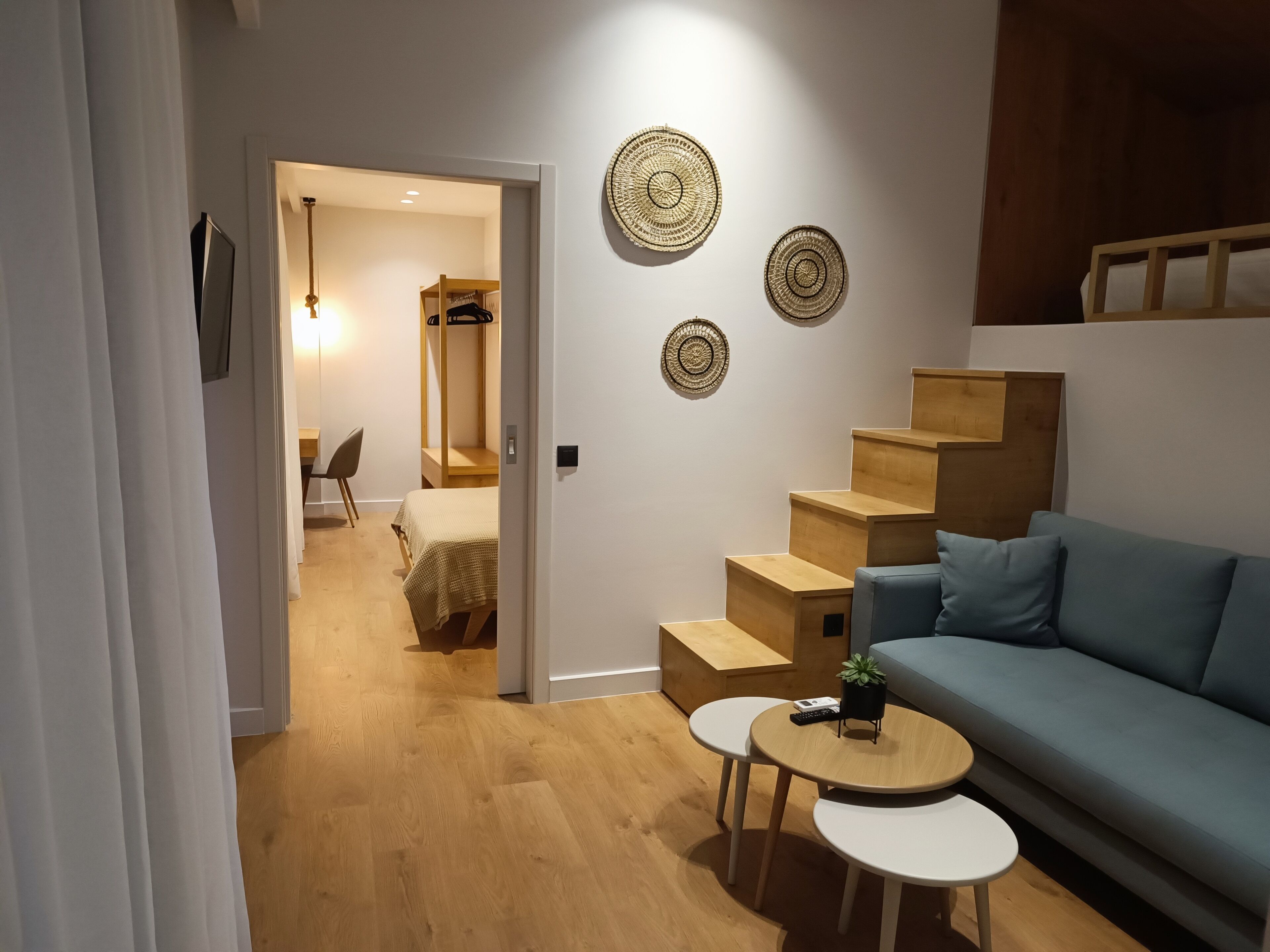 Un saló modern amb un sofà blau, una escala de fusta i una taula rodona petita.