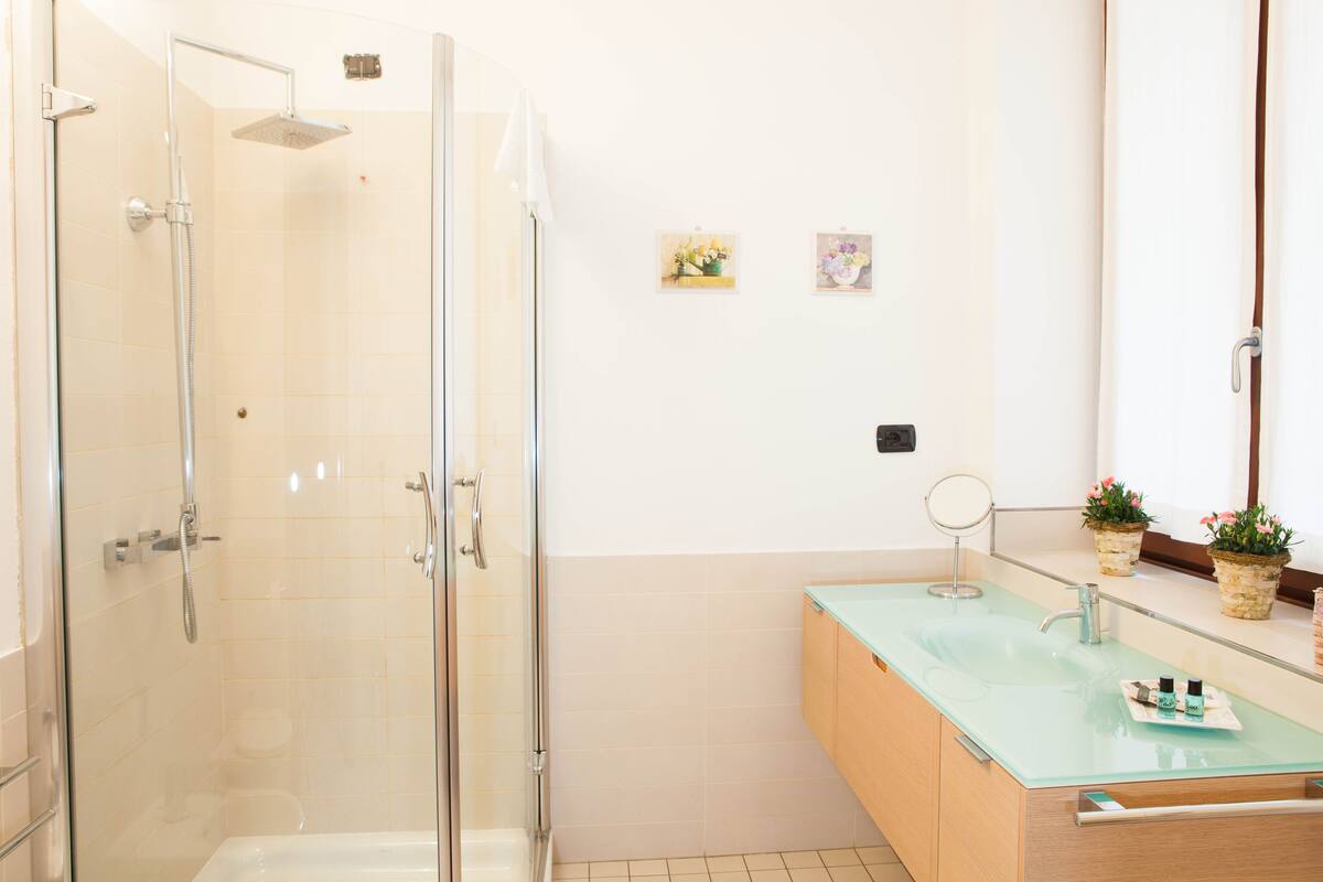 A modern bathroom with a glass shower enclosure, a glass sink, and a wooden vanity.