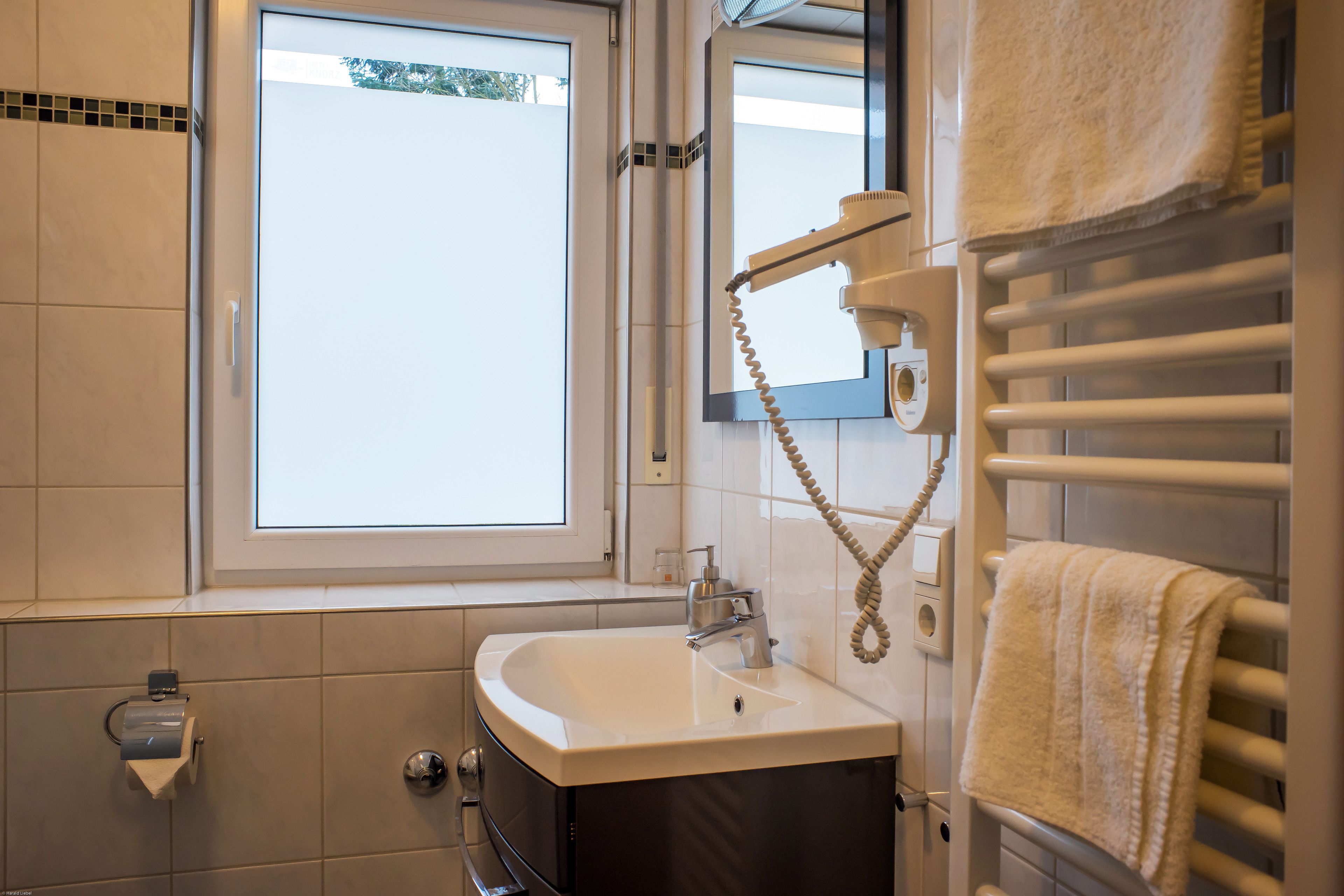 A bathroom with a sink, mirror, towel rack, and window.