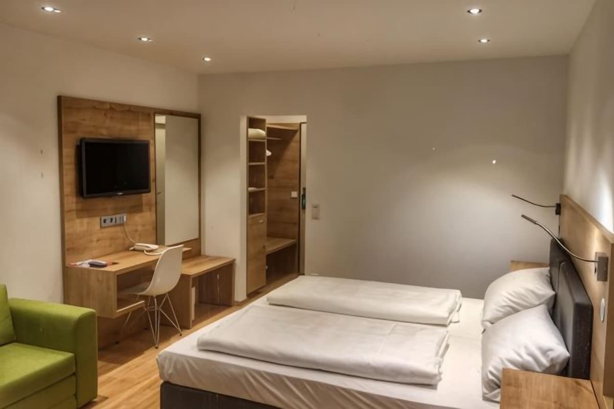 A hotel room with a bed, a desk, a chair, a television, and a wardrobe.