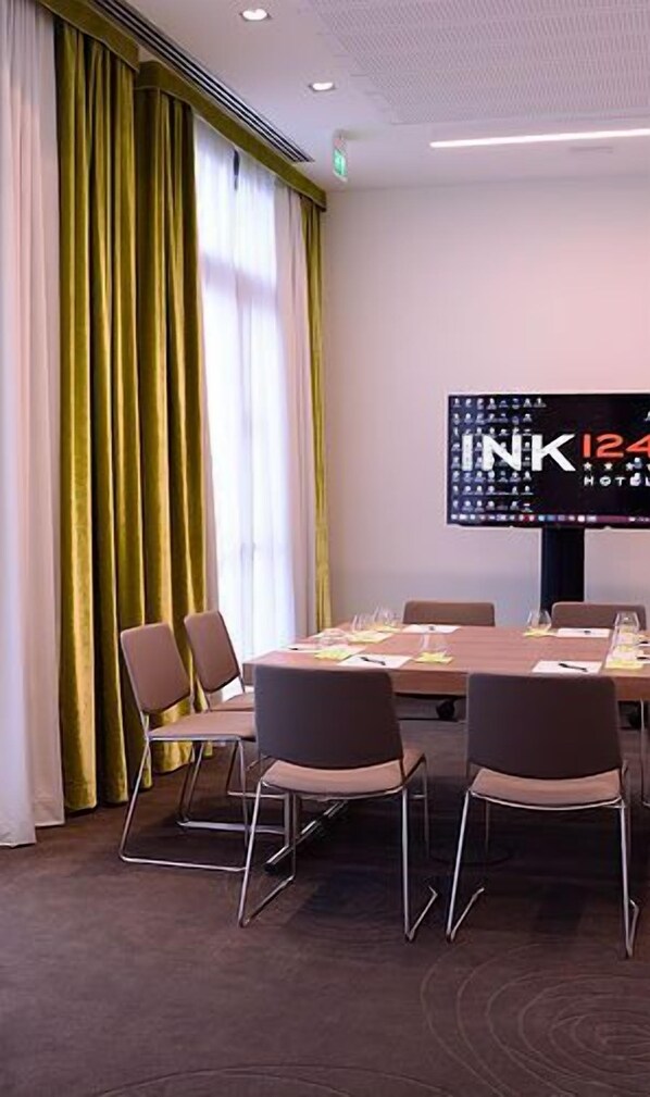 A conference room with a large table, four chairs, and a screen displaying 'INK 124 HOTEL'.