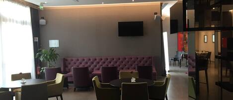 A modern lobby with a seating area, a flat-screen TV mounted on the wall, and a staircase to the right.
