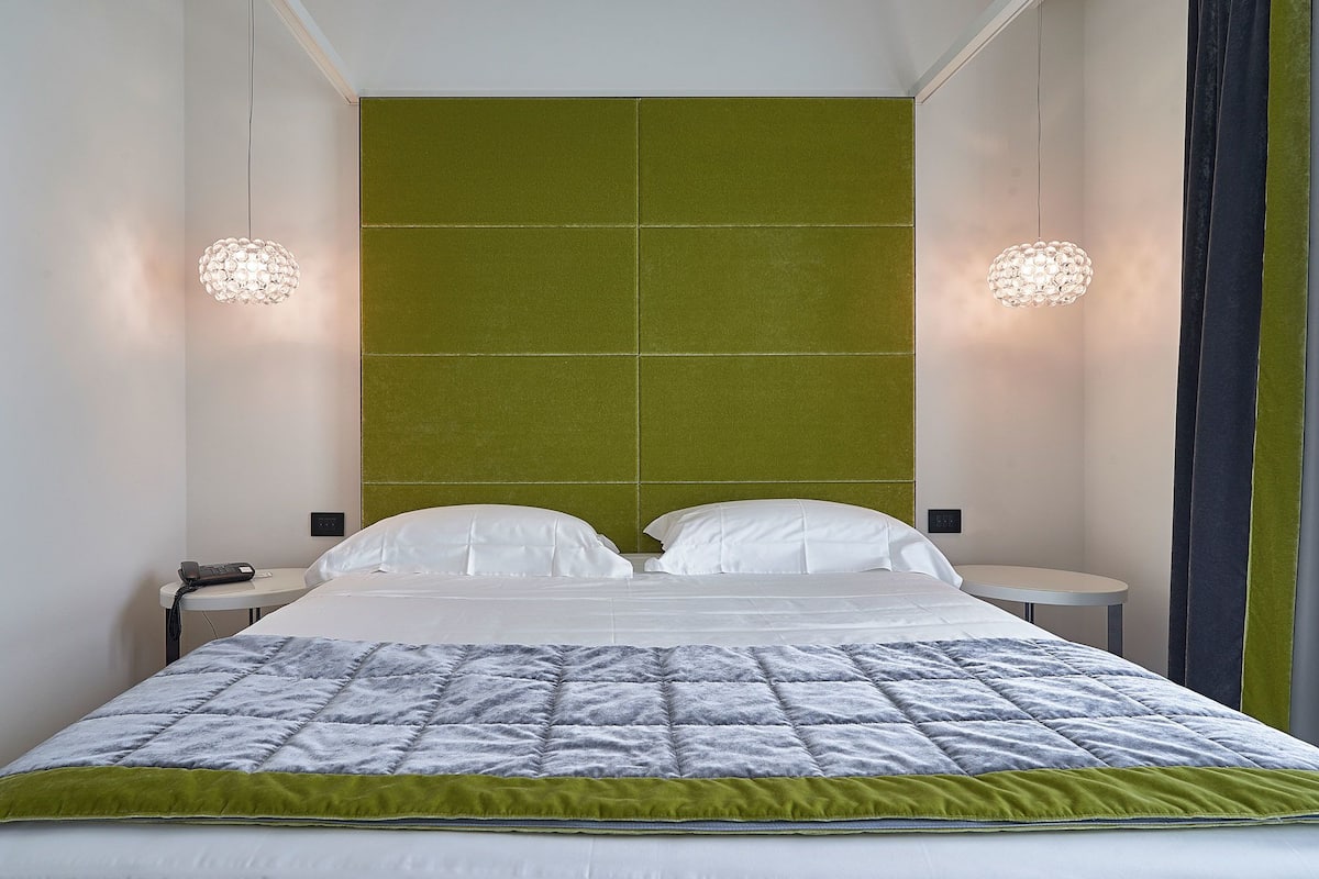 A hotel room with a large bed, two bedside tables, a green accent wall, and two wall-mounted lamps.