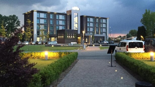 Ein modernes Hotel mit gepflastertem Weg zum Eingang, umgeben von gepflegter Bepflanzung und einem Parkplatz.