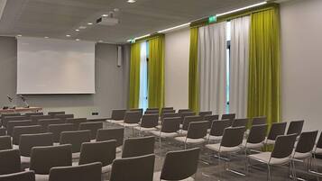 Une salle de conférence avec des rangées de chaises, un écran de projection et un pupitre.