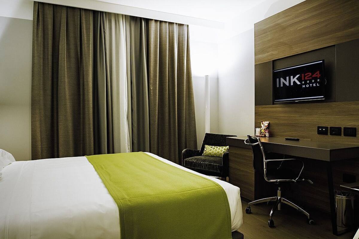 A hotel room with a bed, a desk, a chair, a television, and a sign indicating the hotel name and rating.
