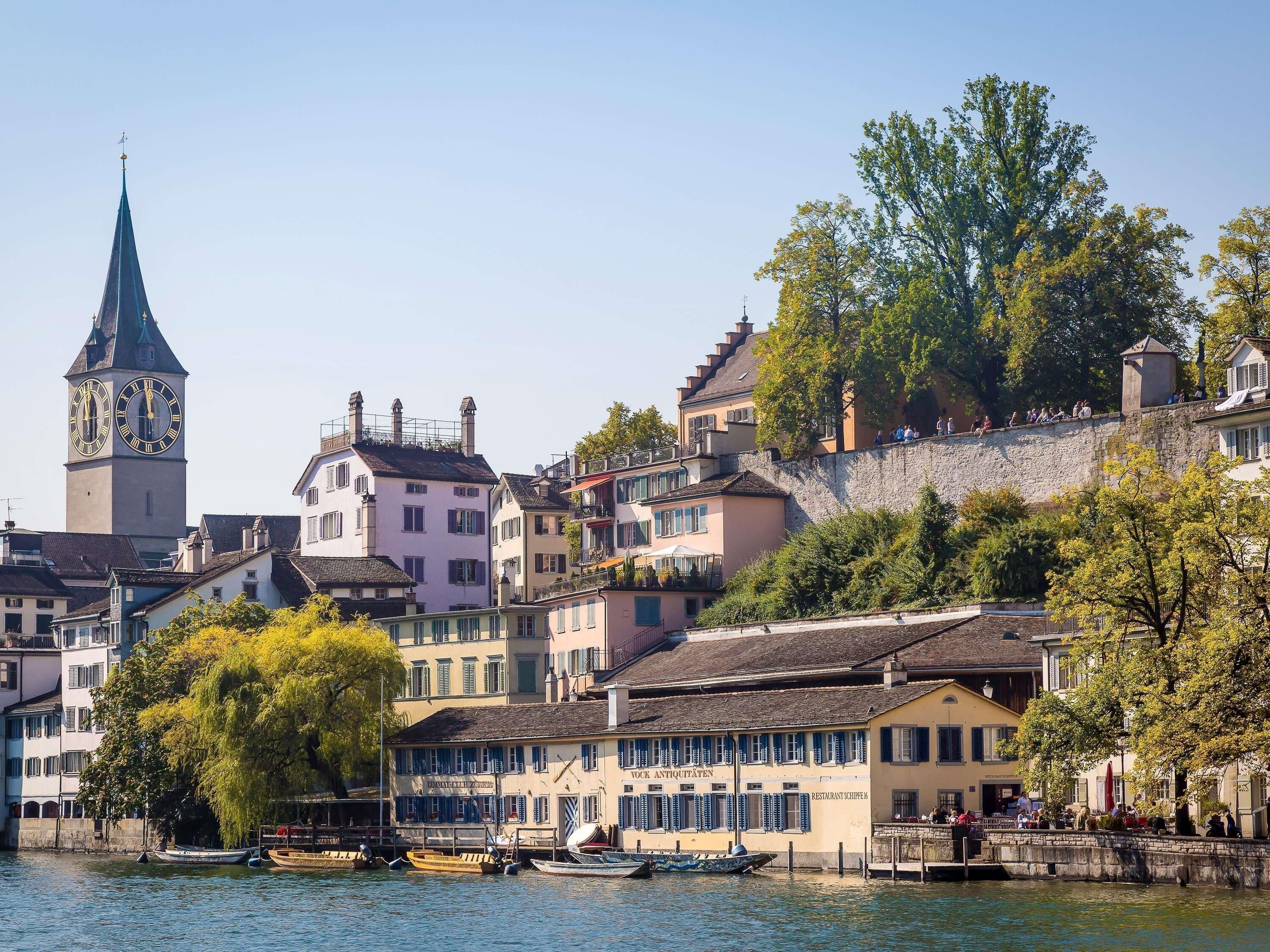 A historic town with a prominent clock tower, traditional buildings, and a river with boats.