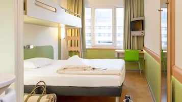 Una habitación de hotel con una cama litera, un escritorio, una silla, un televisor y una ventana con cortinas.