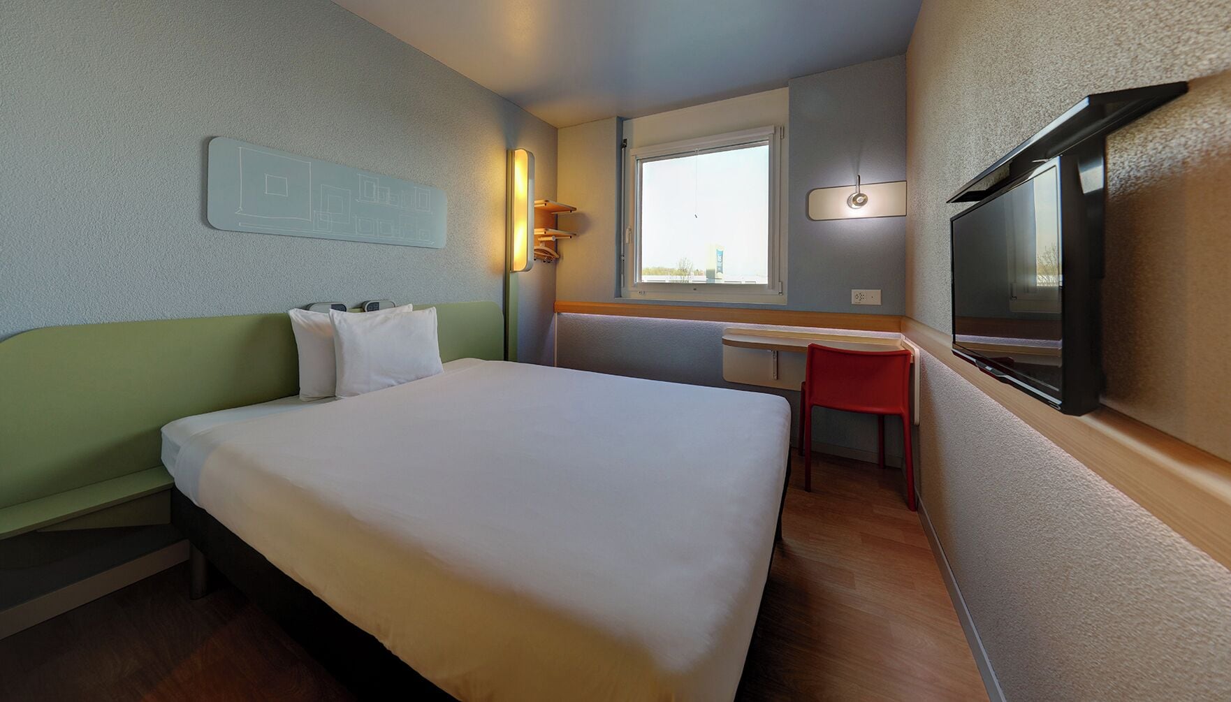 Una habitación de hotel con cama, escritorio, silla, televisor y ventana.