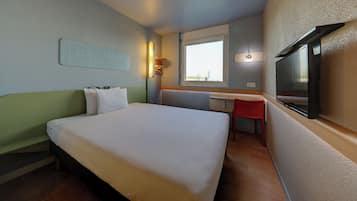 Una habitación de hotel con cama, escritorio, silla, televisor y ventana.