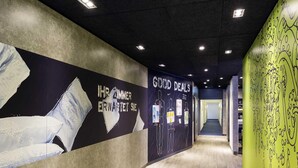 Ein Flur mit einem Wanddesign in Schwarz und Gelb, einem Betonboden und einer Tür am Ende.