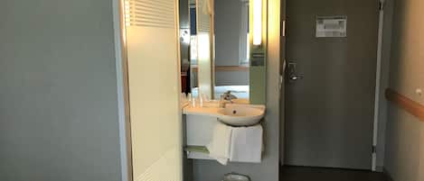 Baño de hotel con lavamanos, espejo, toallero y un cubo de basura.