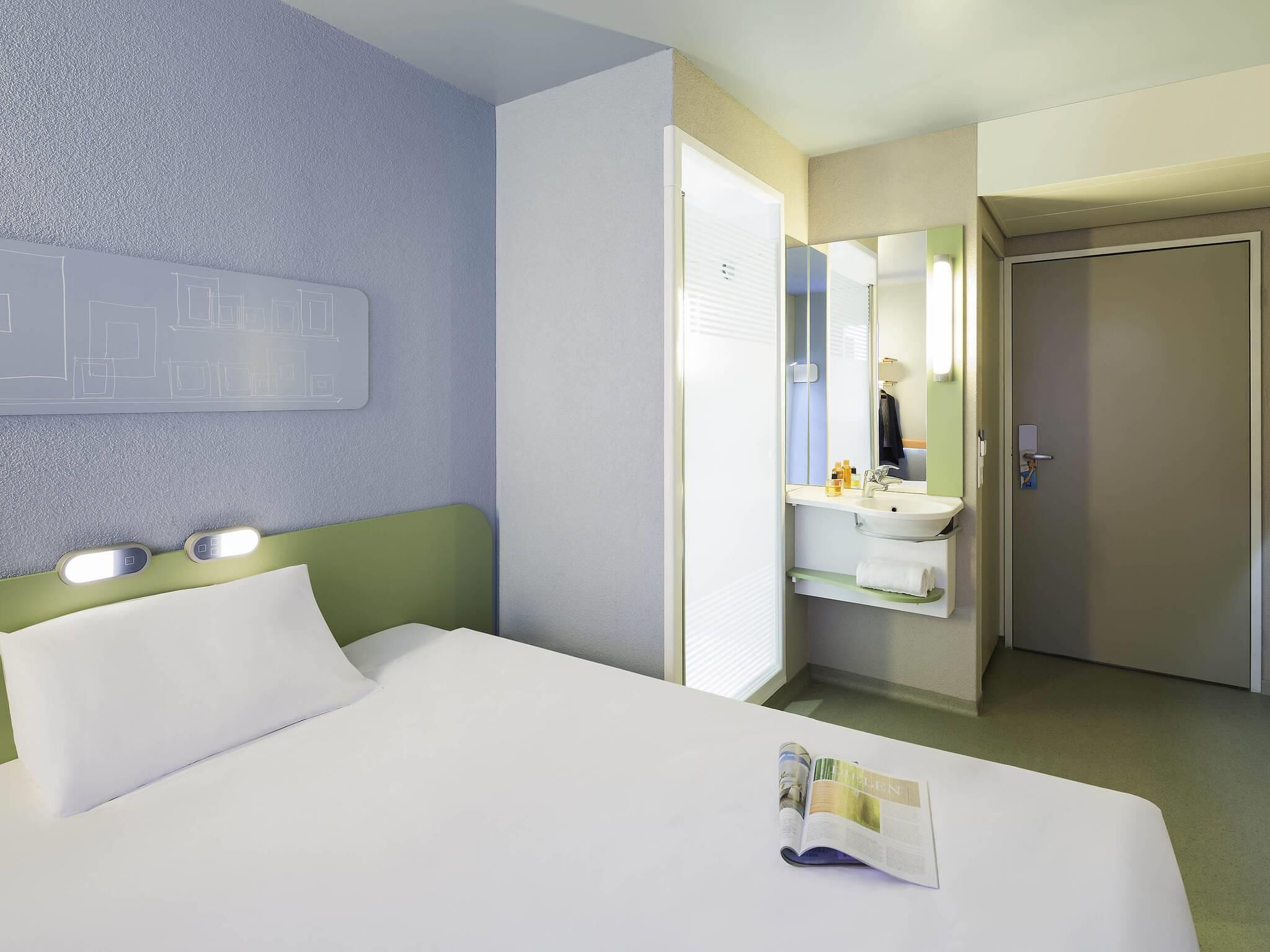 A hotel room with a bed, a bathroom with a mirror, and a magazine on the bed.