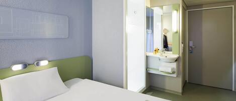 Una habitación de hotel con una cama, un baño con un espejo y una revista sobre la cama.