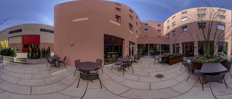 A courtyard with outdoor seating, a building with a curved facade, and a red entrance.
