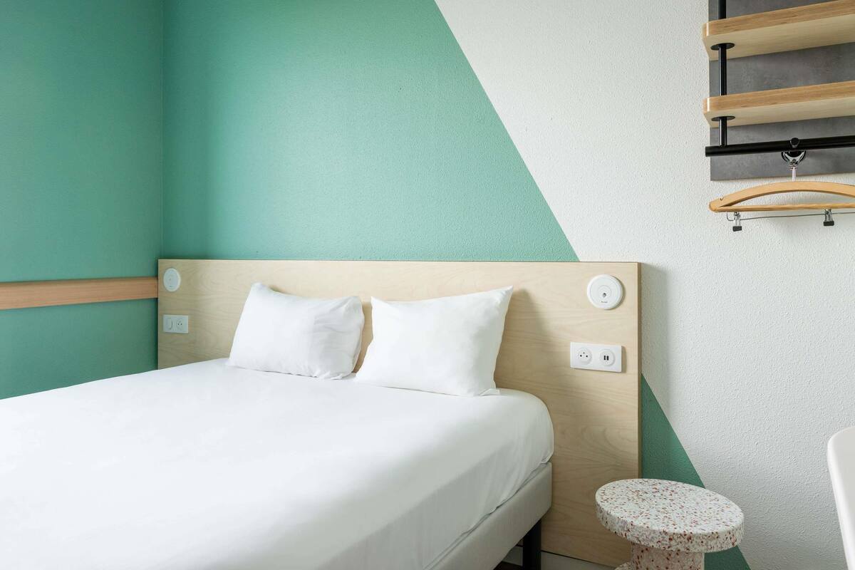 Ein ordentlich eingerichtetes Hotelzimmer mit einem Bett, einem Nachttisch und einem kleinen runden Tisch.