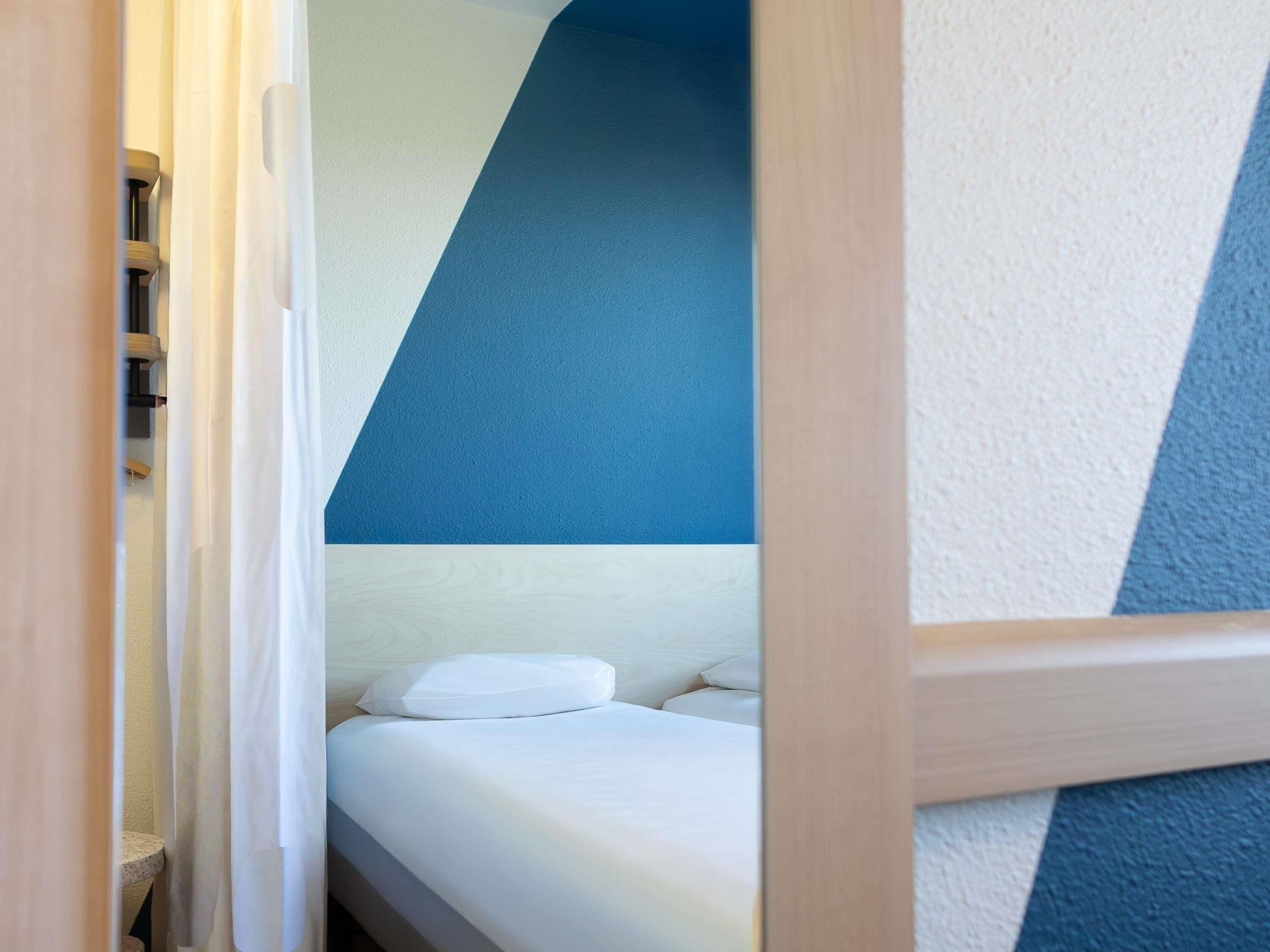 Habitación con cama, techo inclinado y vista parcial de un baño.