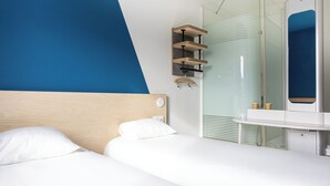 Una habitación de hotel moderna con cama, mesita de noche y cabina de ducha de vidrio.