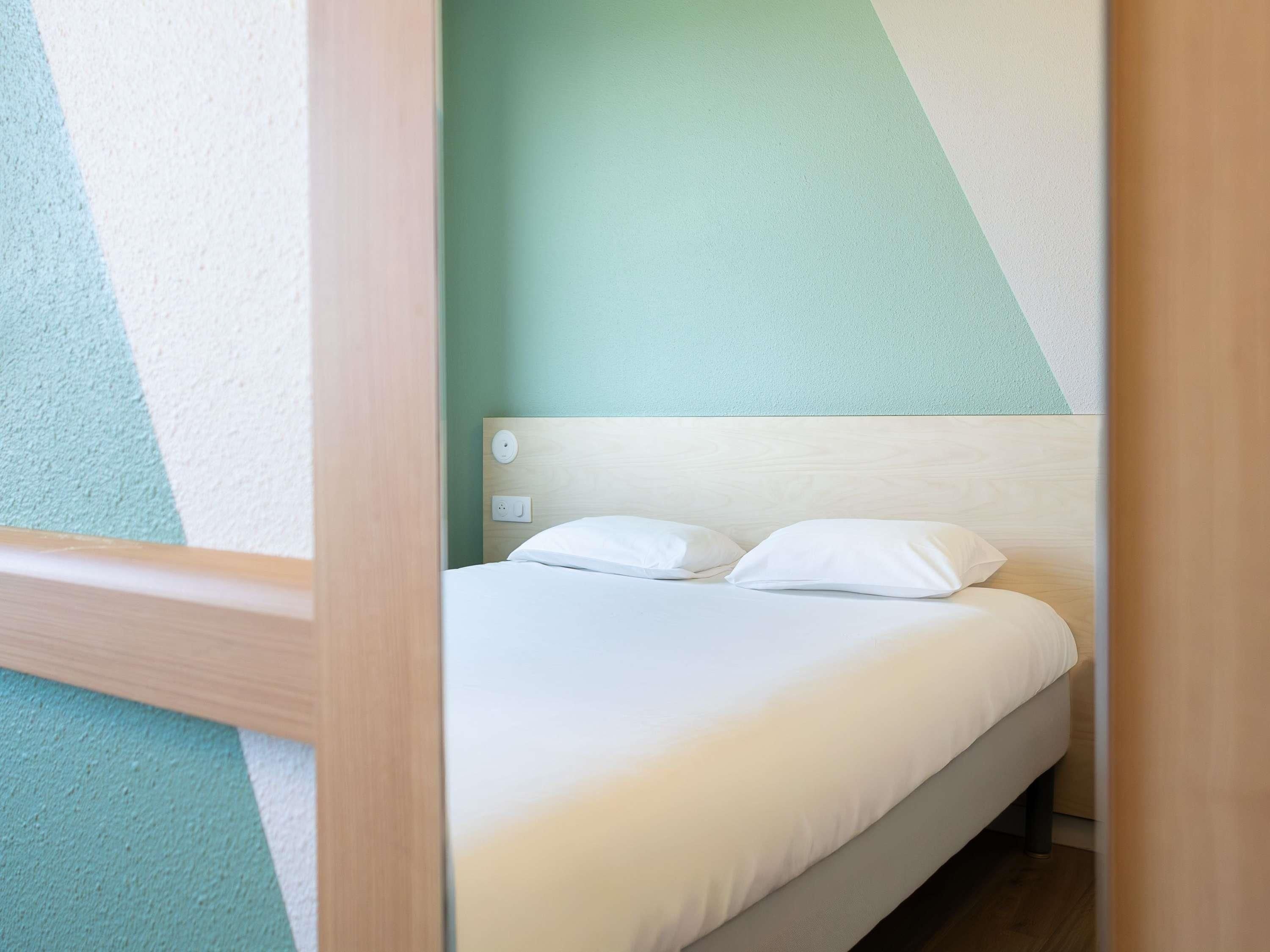 Uma cama de solteiro com roupa de cama branca num quarto com design geométrico na parede.