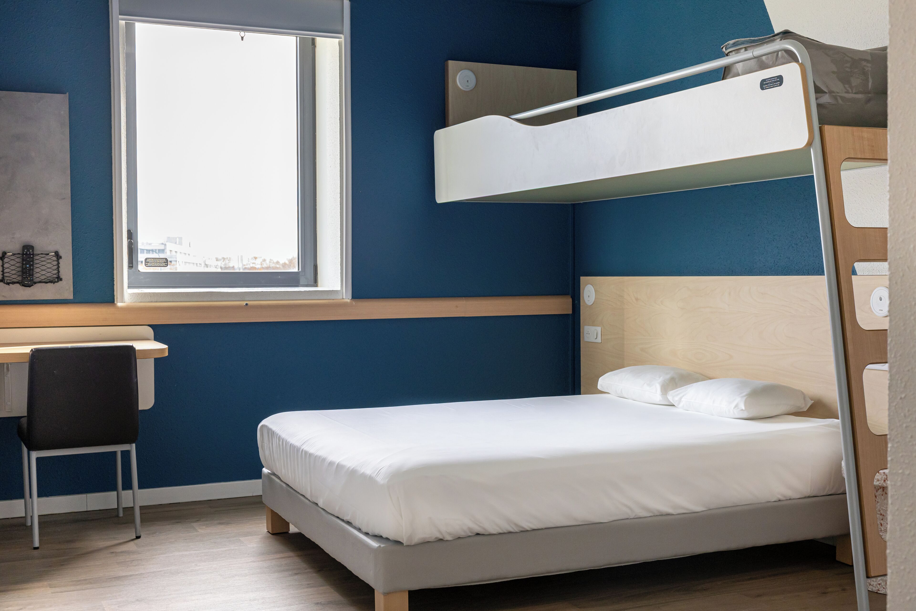 A bunk bed with a desk and chair, a window, and a wall-mounted shelf.