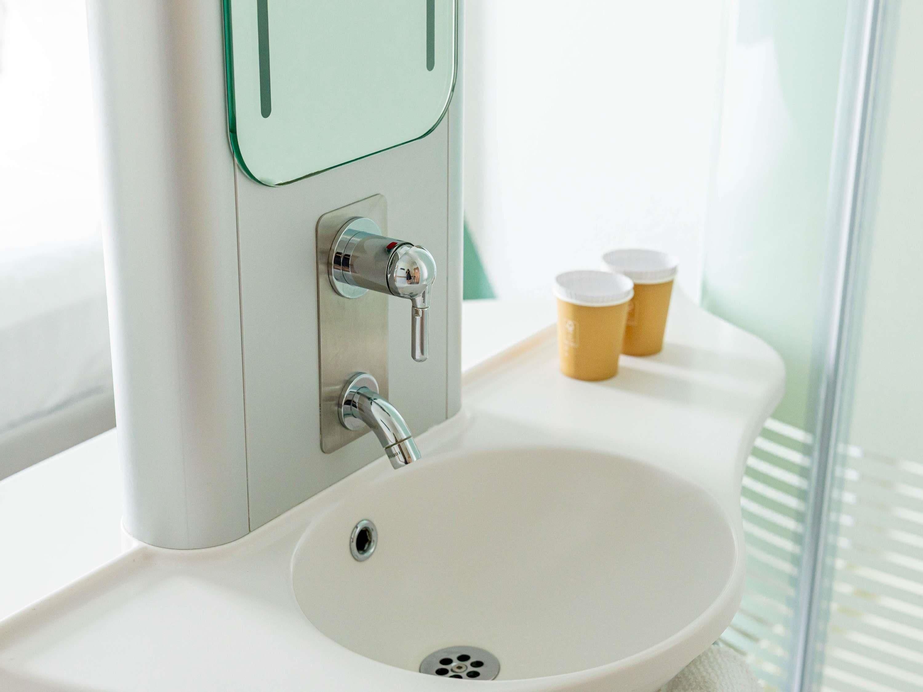 A bathroom with a white sink, a mirror, and two paper cups on a tray.