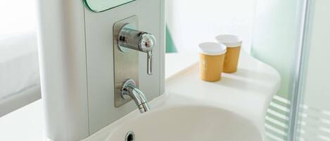 A bathroom with a white sink, a mirror, and two paper cups on a tray.