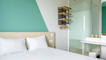 A modern hotel room with a bed, a glass shower, and a wooden shelf unit.