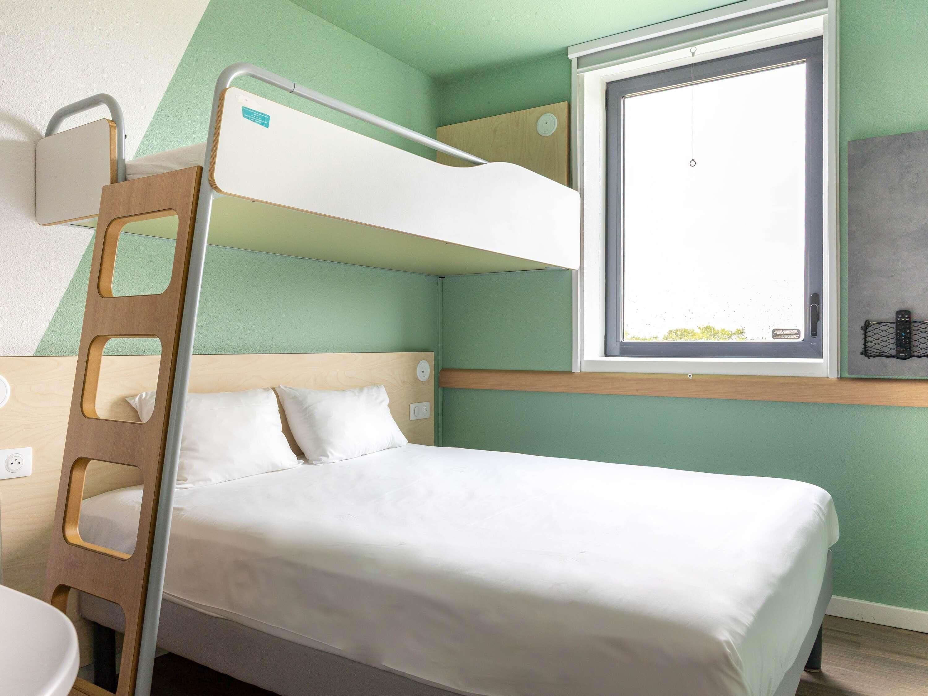 A bunk bed with a ladder, a window with a view, and a bedside table.