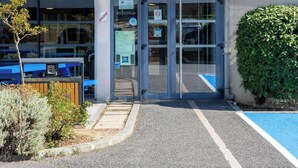 Exterior de un hotel ibis budget en el Aeropuerto de Toulouse, con acceso de vidrio, un letrero azul y una pequeña zona ajardinada.