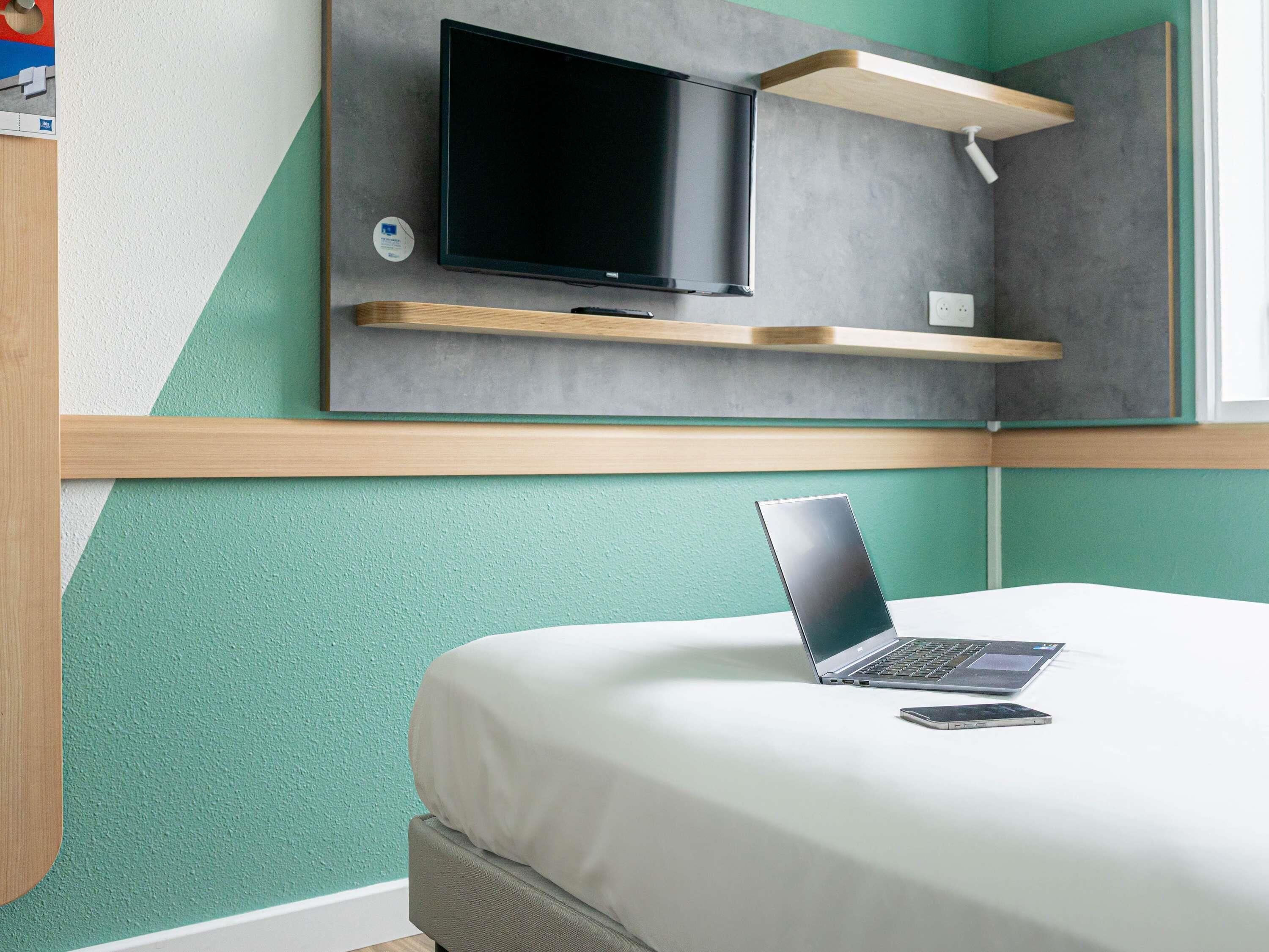 A modern bedroom with a bed, a laptop, a TV, and built-in shelves.