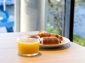 A breakfast setting with croissants and orange juice on a table by a window. - ibis budget Toulouse Blagnac Aéroport (Blagnac)