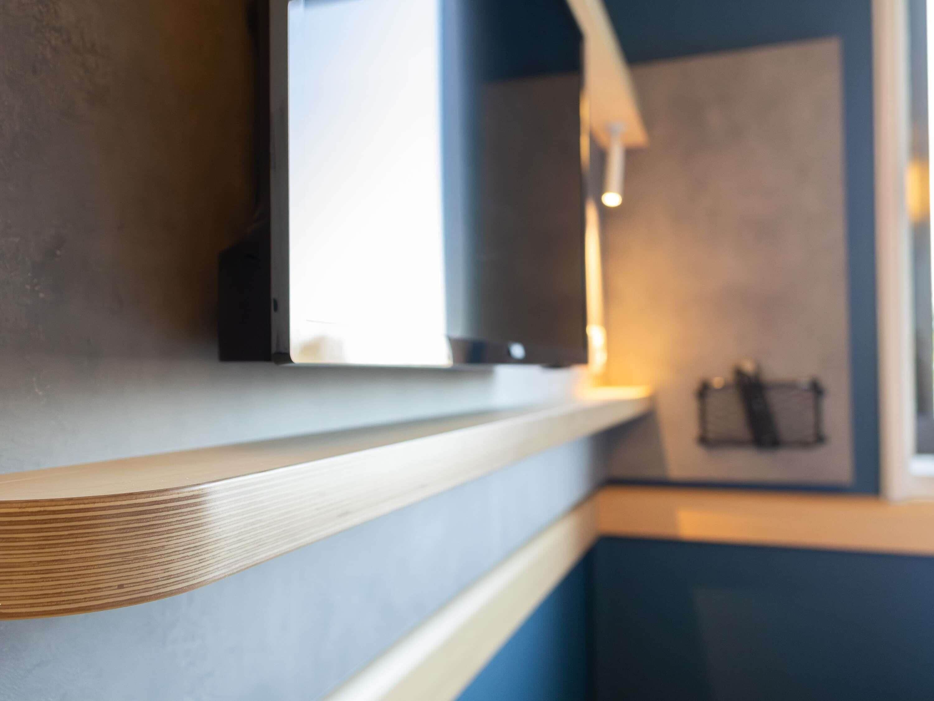 Un intérieur moderne avec un comptoir en bois, un téléviseur fixé au mur et une porte de couleur foncée.