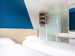 Una camera d'albergo con un letto, un comodino, uno specchio e un angolo doccia.