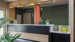 A reception desk with a wooden panel, a potted plant, and informational posters.