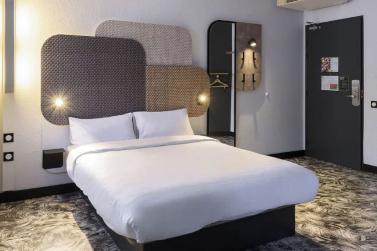 A modern hotel room with a large bed, a wall-mounted mirror, and a door with a lock and a small sign.
