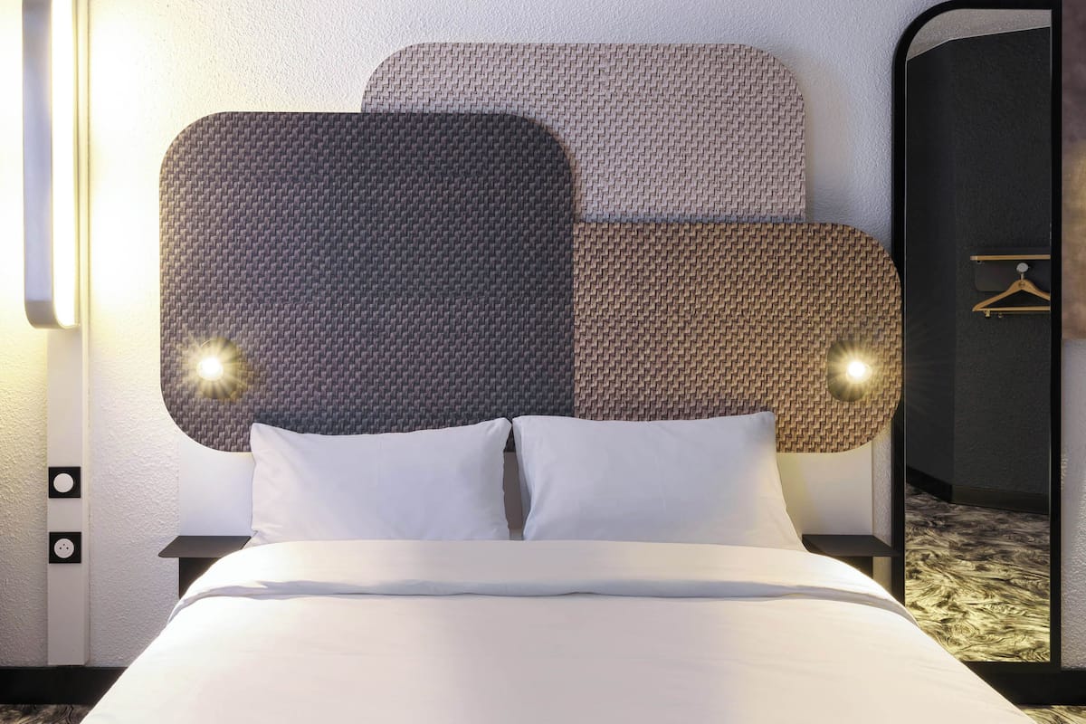 A hotel room with a large bed, a headboard with a textured design, and a wall-mounted light fixture.