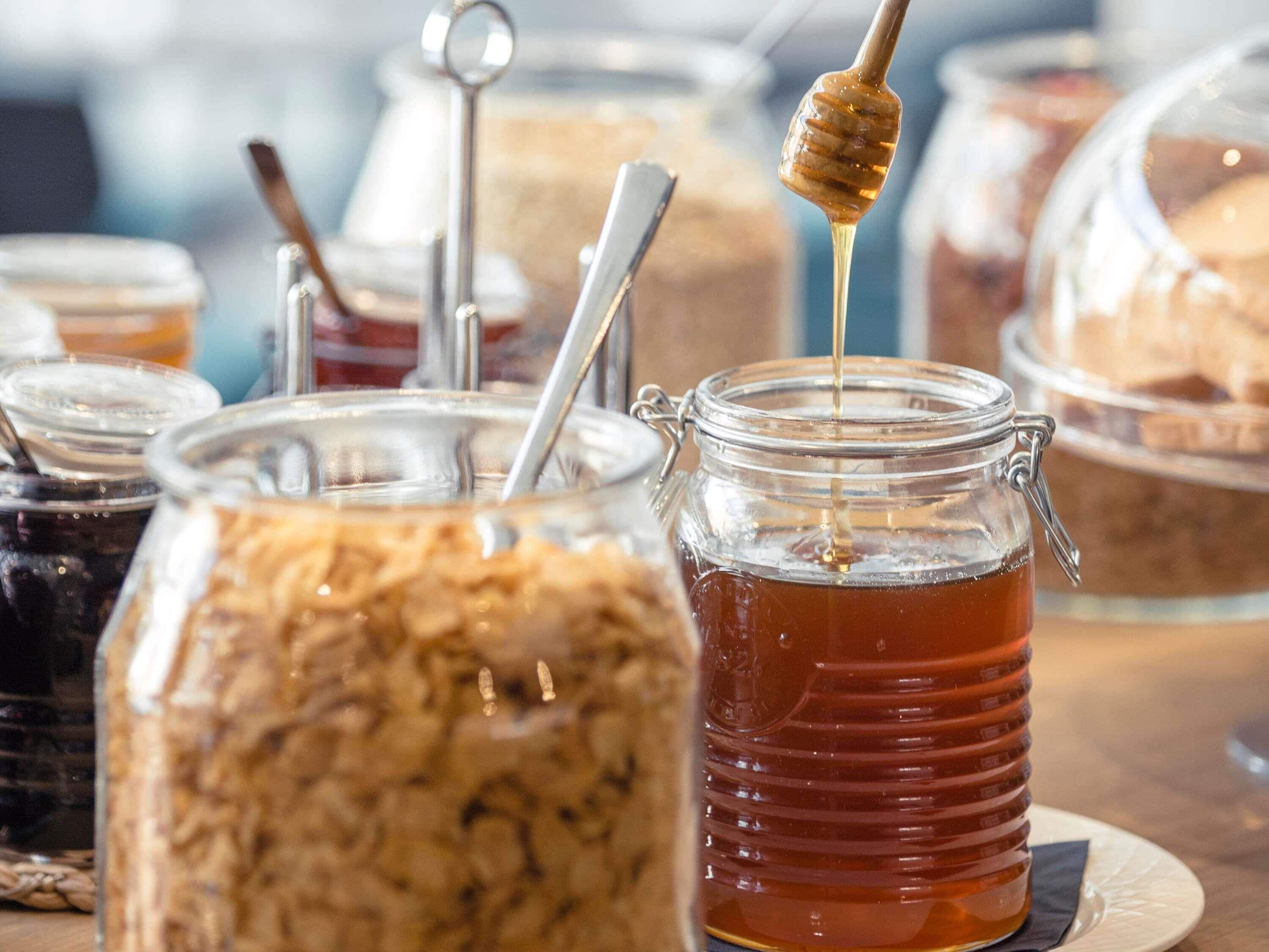 On peut voir divers aliments présentés dans des récipients en verre, notamment du miel et ce qui semble être un pot de confiture.