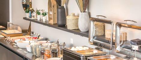 A buffet setup with various food items, a coffee machine, and decorative items on shelves.