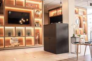A modern interior with a large flat-screen TV, built-in shelves with decorative items, a black refrigerator, and a small table with a vase.