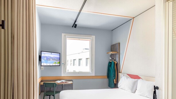 Hotellihuone, jossa on sänky, työpöytä, tuoli, televisio ja ikkuna, josta on näkymä rakennuksiin.