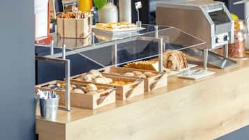 A bakery display with various baked goods, a coffee machine, and a plant.