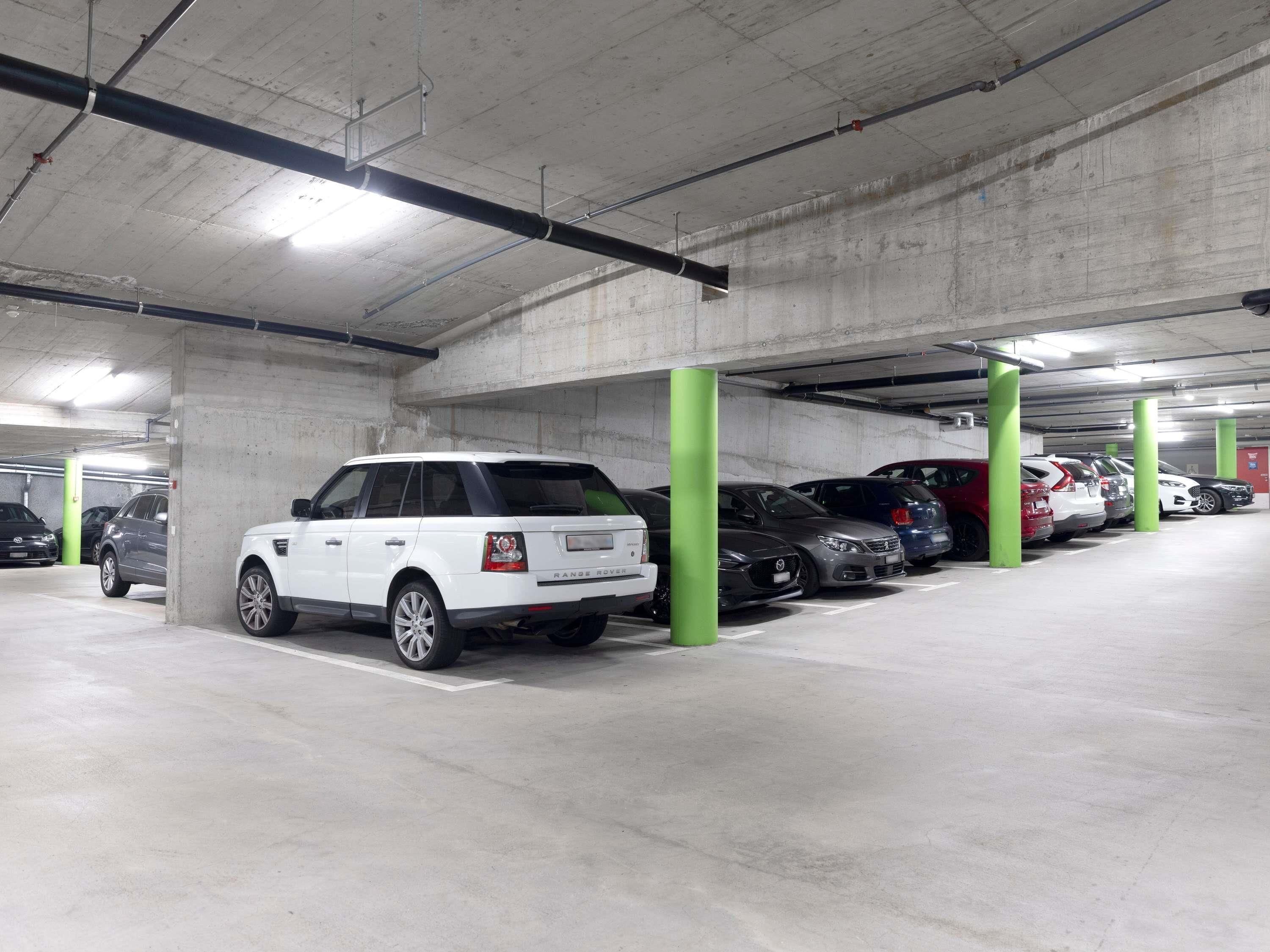 A parking garage with concrete pillars, multiple cars parked, and overhead lighting.