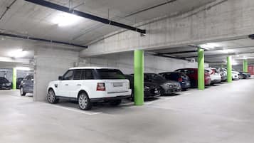 Un garaje para estacionar con pilares de hormigón, varios coches aparcados e iluminación superior.
