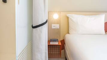 Una camera d'albergo con un letto, un comodino, un libro, una lampada e un telefono fissato al muro.
