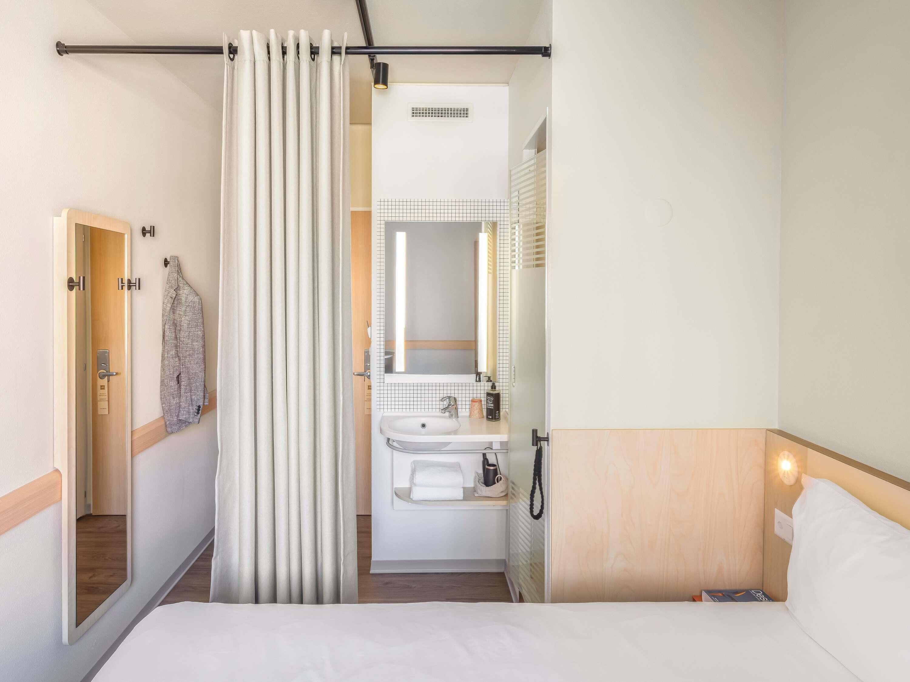 A hotel room with a bed, a bathroom with a sink and mirror, and a shower curtain.